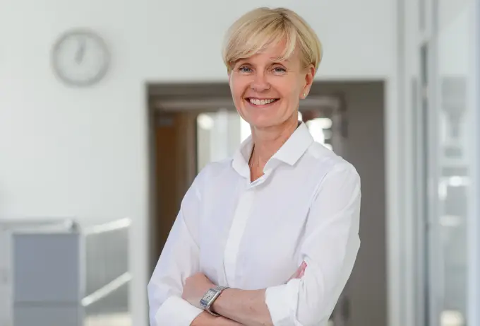 A smiling business woman in a white shirt standing in an office.